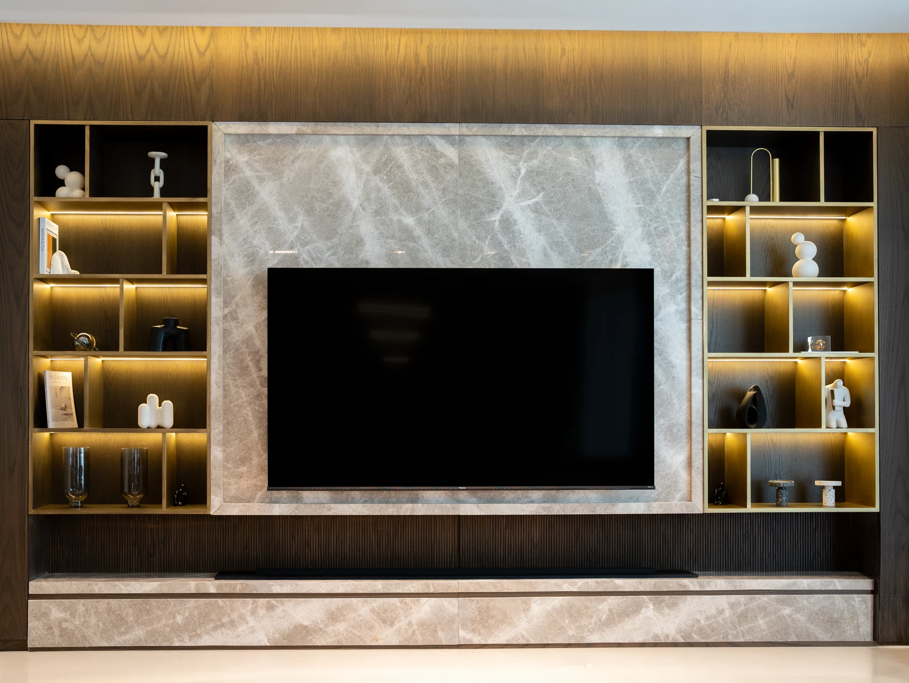 A marble media wall framed by illuminated display cabinetry and dark wood millwork
